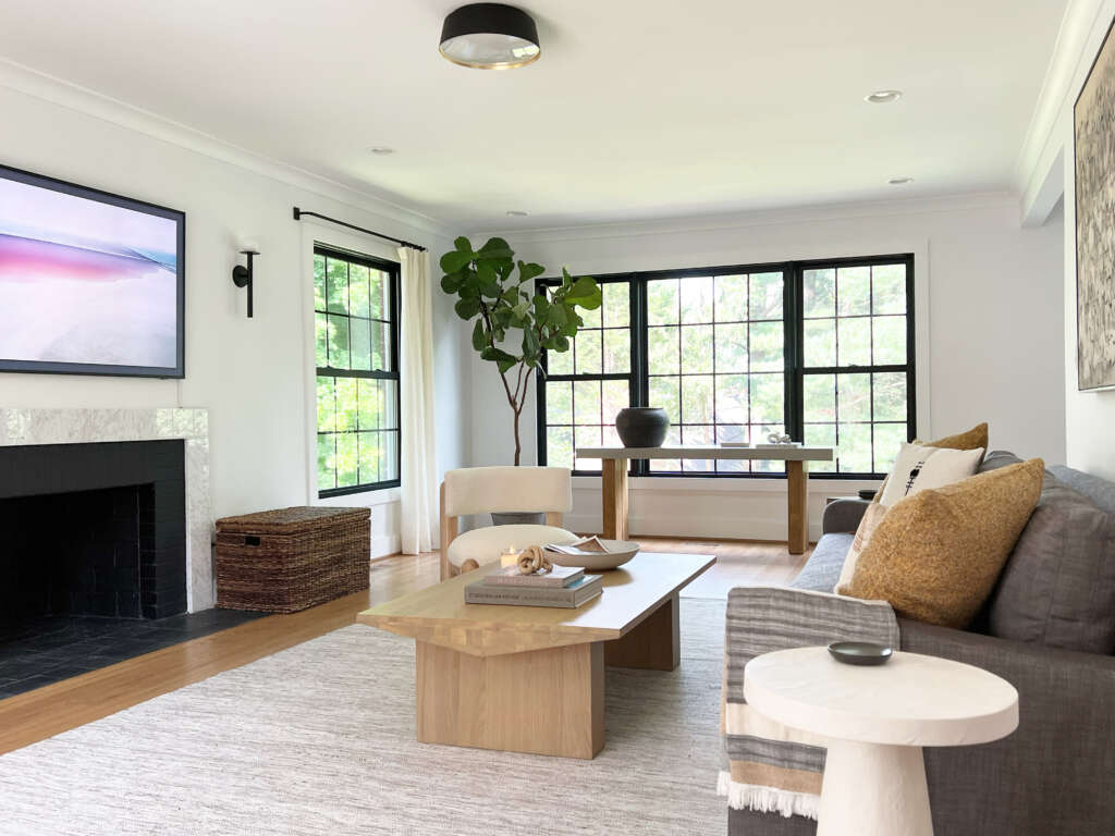 Modern living room with black-framed windows, neutral furniture, and a minimalist design featuring a marble fireplace and natural wood accents.