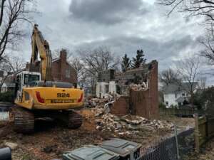 Excavator demolishing an old brick home in Arlington, VA during the initial phase of a custom home build.