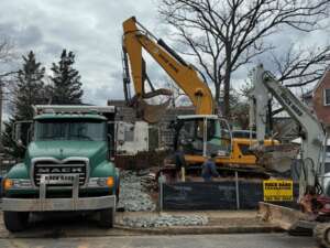 Excavators and a dump truck clearing rubble from a demolished home in preparation for a custom home project.