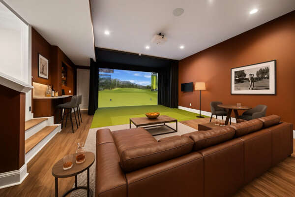 Custom basement golf simulator and lounge with leather seating, bar area, and theater-style setup designed by Paradigm Homes